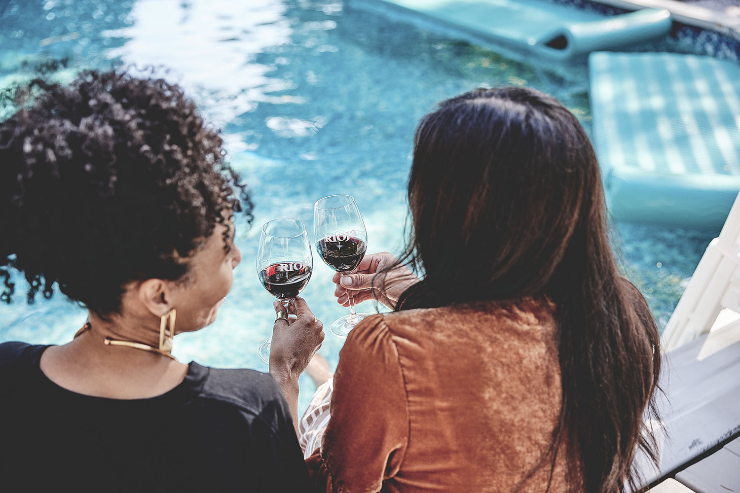 Bild von zwei Frauen die am Pool ein Glas Rioja Rotwein miteinander geniessen.