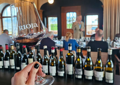 Foto von einem Weinglas mit Rioja Logo. Im Hintergrund David Schwarzwälder und die Weine aus der Verkostung im Mammertsberg.