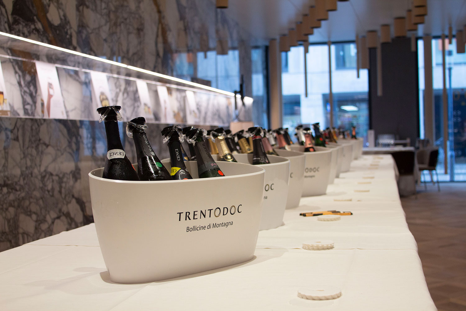 Schaumweinflaschen in Eiskübel mit dem Trentodoc-Logo aufgestellt auf einem langen Tisch.