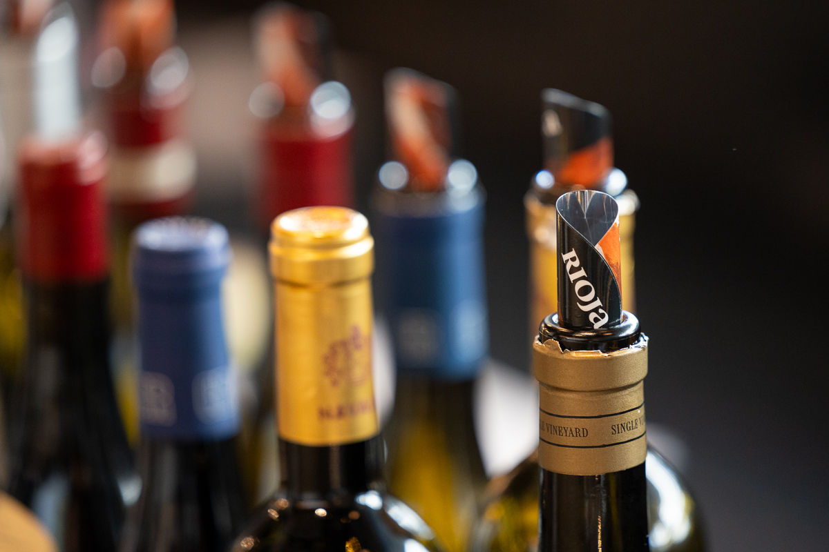 Mehrere Weinflaschen mit Rioja-Kapseln auf einem Tisch, eine Flasche im Vordergrund scharf fokussiert, Hintergrund unscharf.